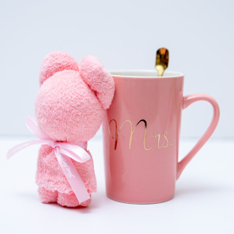 A pink teddy bear next to a pink mug with "Mrs" in gold, gold spoon inside.