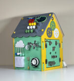 Multifunctional activity house toy with various interactive parts including a clock and knobs, viewed from another side on a grey background.