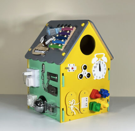 Multifunctional activity house toy with various interactive parts including a clock and knobs, viewed from another side on a grey background.