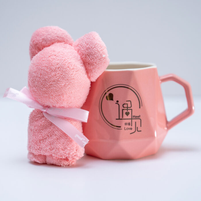 Elegant pink mug with character design accompanied by a plush teddy bear, a gold spoon, and a pink flower on a pink background