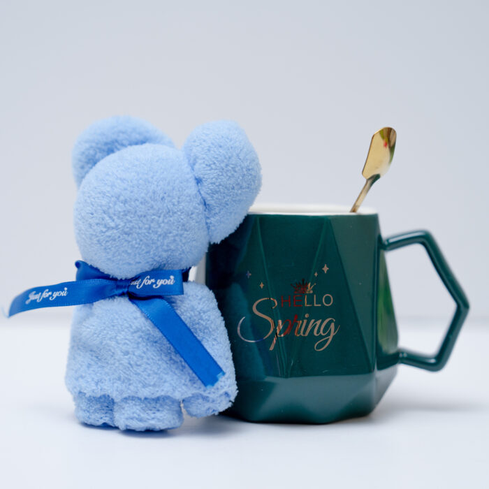 Dark green mug with 'Hello Spring' print, accompanied by a blue teddy bear and a gold spoon, on a white background.