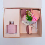 "Elegant gift box containing a pink home fragrance bottle and a small bouquet of pink flowers, neatly tied with a ribbon.