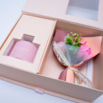 Luxurious pink gift box with home fragrance and a floral bouquet, perfect for gifting, displayed on a pink surface.