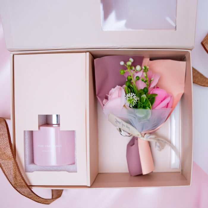 Luxurious pink gift box with home fragrance and a floral bouquet, perfect for gifting, displayed on a pink surface.