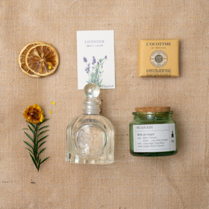 "Flat lay of aromatherapy items including dried orange slice, lavender card, bar soap, glass perfume bottle, and a jar candle on a white background." "Flat lay of aromatherapy items including dried orange slice, lavender card, bar soap, glass perfume bottle, and a jar candle on a burlap background